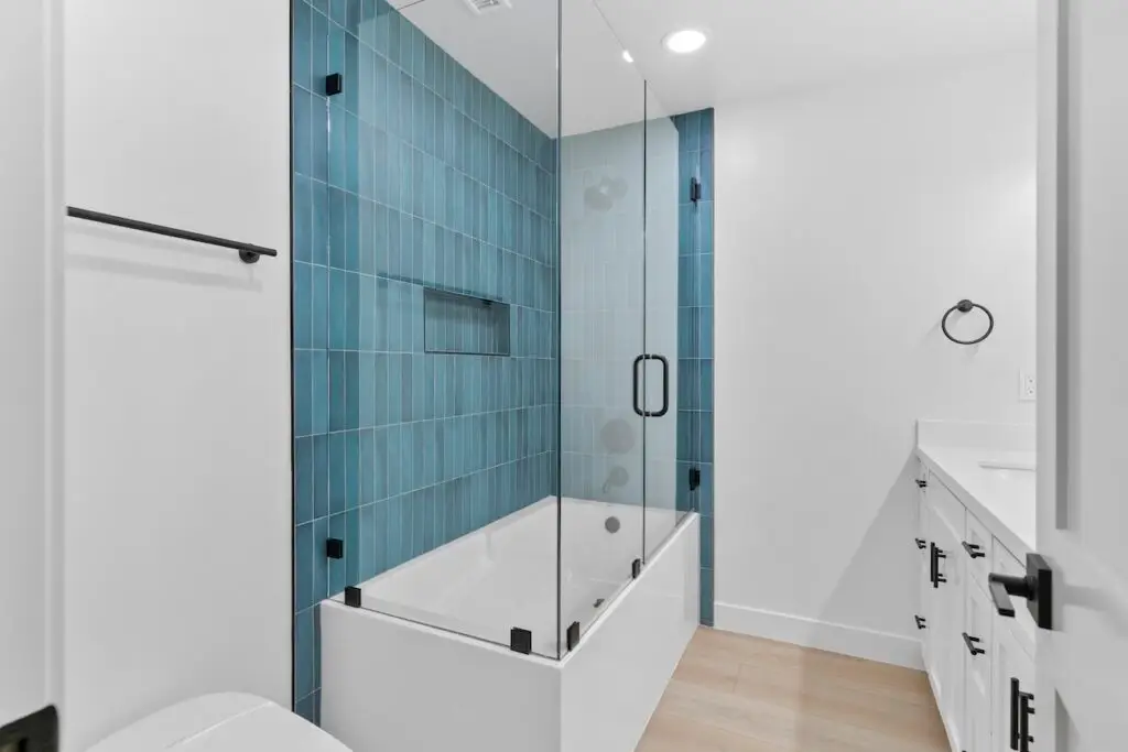 Bathroom remodeling in Plano, TX, with a blue-tiled shower, glass enclosure, and white cabinetry, blending contemporary style with functional elegance.