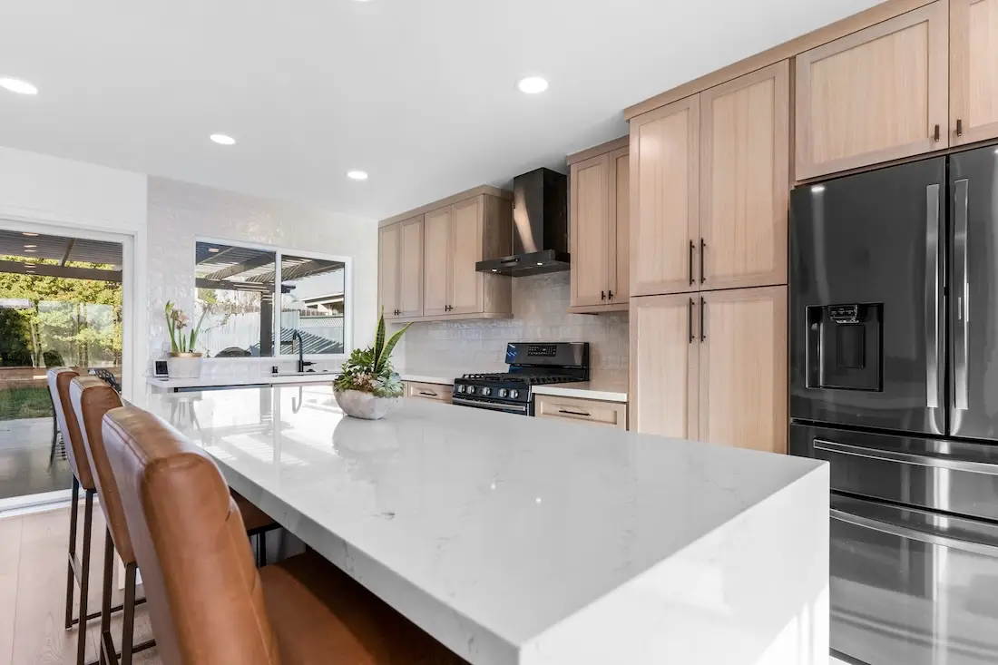 Kitchen remodeling in Dallas, TX, featuring a modern open-concept design with a sleek black and wood-tone island, high-end appliances, and stylish leather bar stools for a warm and contemporary space
