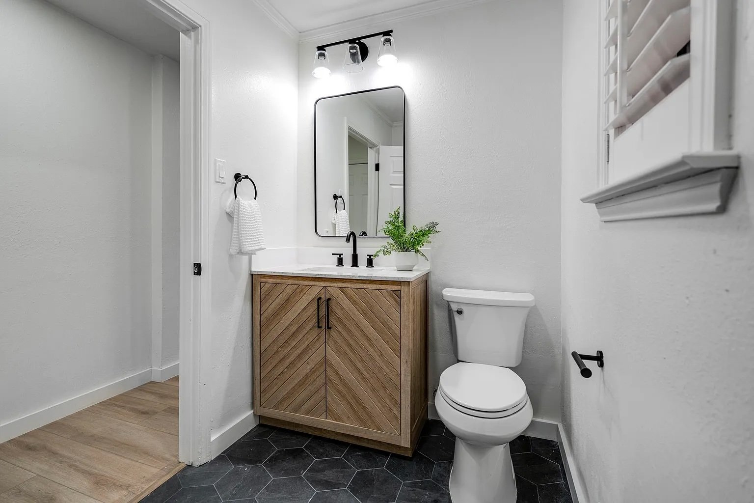 Minimalist bathroom remodel in Addison, TX with a wooden vanity, modern lighting, and black matte fixtures